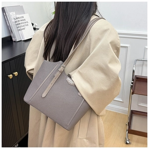 Detail of grey leather tote bag with fashion label and adjustable strap on a beige coat