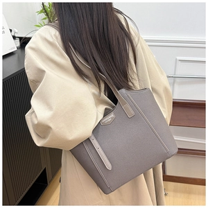Close-up of a large grey textured tote bag worn over the shoulder with a beige trench coat