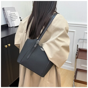 Detail of black pebbled leather tote bag with silver buckle strap worn with a beige coat