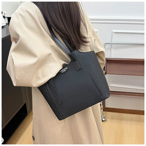Detail of black leather tote bag with long shoulder straps on a light trench coat
