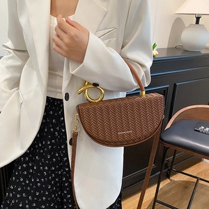 Sacoche marron tressée avec poignée dorée portée par un mannequin en tenue chic