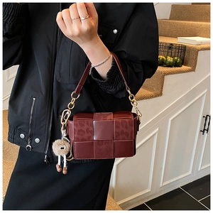 Detail of burgundy woven leather handbag featuring leopard print patterns and a fuzzy charm