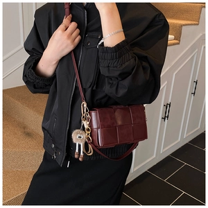 Detailed view of dark red woven leather crossbody bag with a plush owl charm accent