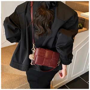 Detail of dark red woven leather crossbody bag with chic pompom charm and gold metal hook