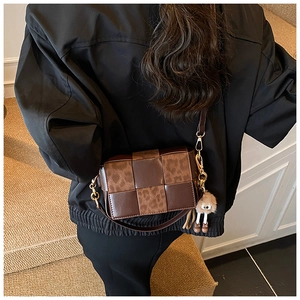 Detailed view of woven brown leather shoulder bag with leopard print and plush charm