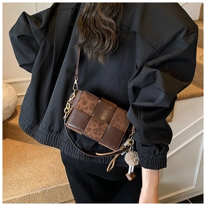 Detail of a brown woven crossbody bag with leopard print accent and gold chain strap