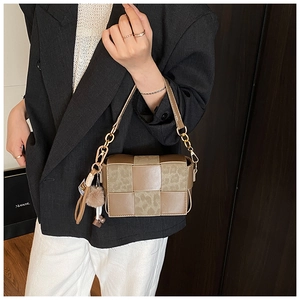 Close-up of woven crossbody bag with leopard print, gold chain, and pompom charm detail