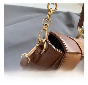 Macro view of gold metal hooks and dual-texture brown leather on a vintage woven bag
