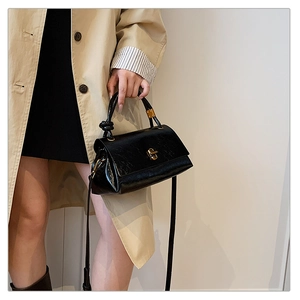 Detail of black glossy handbag with gold twist lock and stylish knotted handle design