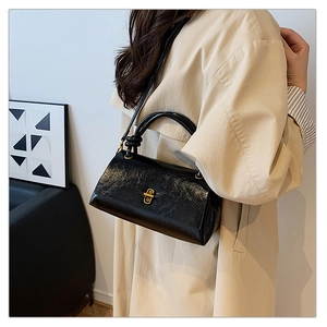 Close-up of black wrinkled glossy leather handbag with gold metal clasp on model