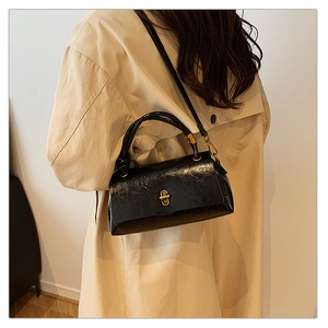 Detail of black glossy pleated handbag with vintage gold turn-lock and tube handle