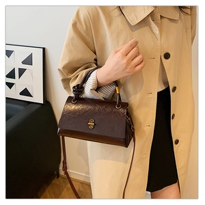 Detail of dark brown faux crocodile leather bag with gold buckle and knotted top handle