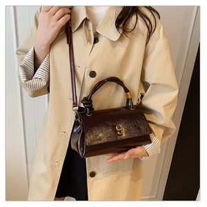 Detail view of a vintage dark brown satchel bag with a gold twist-lock on beige trench coat