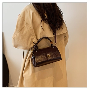 Detail of dark brown glossy leather handbag with twist handle and metal clasp closure
