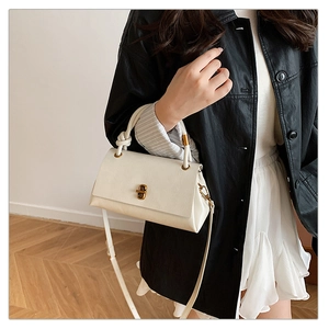 Close-up of white minimalist crossbody bag with gold twist lock and knotted handle detail