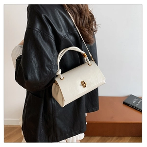 Detail of off-white crossbody bag with gold metal twist lock and textured leather finish