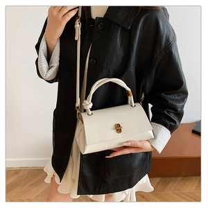 Close-up of a white leather crossbody bag with a unique knot handle and gold buckle