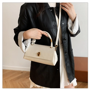 Detail of a creamy white leather handbag with gold twist lock and adjustable shoulder strap