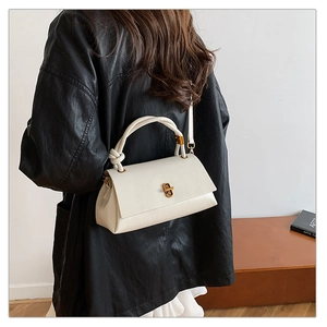 Detail of cream white handbag featuring a unique knotted handle and vintage gold twist lock
