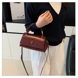 Detail of burgundy glossy handbag featuring a unique knotted handle and vintage gold lock