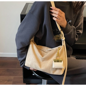 Macro detail of beige suede hobo bag with leather strap and decorative mini charm