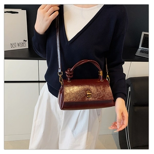 Detail of burgundy textured leather crossbody bag with gold twist-lock and knotted handle
