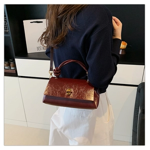 Detail of dark red glossy wrinkled leather crossbody bag with golden twist lock