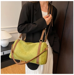 Détail du sac cylindre vert avec bandoulière en cuir brun porté sur un blazer noir