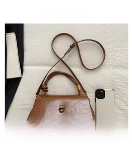 Detailed top view of a brown envelope handbag with gold lock next to a smartphone