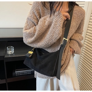 Detail of black suede hobo bag featuring wide leather strap and gold buckle on a model