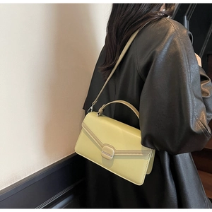 Détail du sac à main vert pistache avec rabat rectangulaire et fermoir sur tenue noire élégante