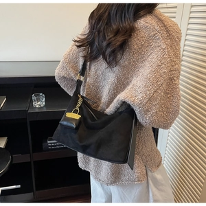 Detail of black faux suede tote bag with mini charm and gold chain on a brown sweater