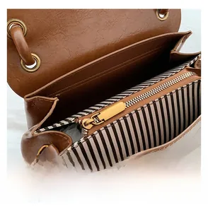 Detail of smooth golden metal zipper and striped lining on brown crossbody bag