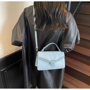 Sac à bandoulière bleu clair porté à l'épaule devant un escalier en bois de luxe
