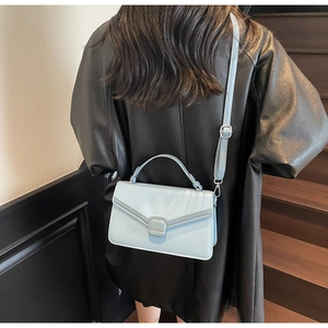 Gros plan d'un sac bandoulière en cuir bleu clair porté sur un manteau en cuir noir