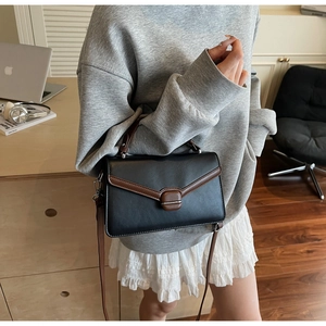 Détail du sac bandoulière bicolore montrant la sangle en cuir marron et le fermoir métal