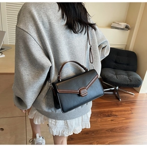 Détail d'un sac bandoulière vintage noir et marron porté par une femme élégante