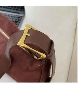Close-up of brown suede shoulder bag featuring a gold triangular buckle and smooth leather