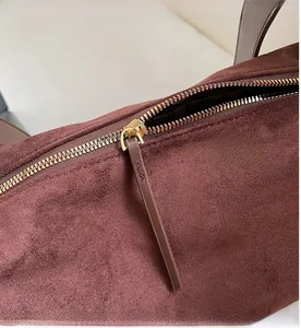 Detail of smooth gold zipper and long suede puller on dark brown underarm bag