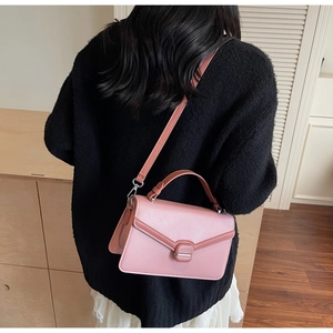 Gros plan d'un sac bandoulière rose avec rabat en V et boucle carrée porté par un mannequin