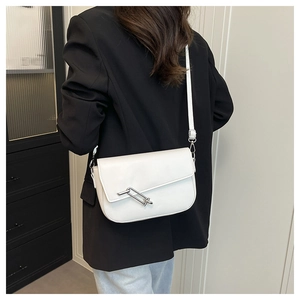 Detail van witte leren crossbody tas met zilveren gesp gedragen op zwarte blazer