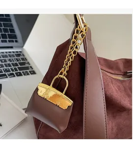 Close-up of brown leather mini bag charm with gold buckle on a suede tote bag