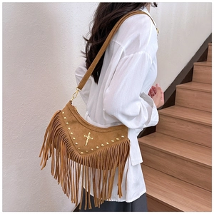 Brown suede crossbody bag with fringe, rivets, and cross charm worn by a model