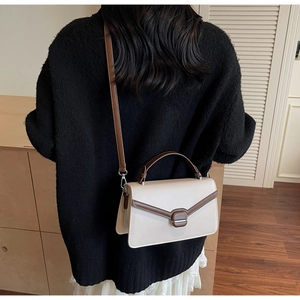 Modèle portant un sac bandoulière bicolore avec bandoulière réglable dans un décor chaleureux