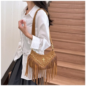Detail view of brown suede shoulder bag with cross pendant, rivets, and long fringe tassels