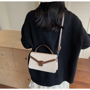 Sac carré bandoulière crème avec bordure marron foncé et poignée porté par un mannequin