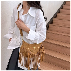 Close-up of brown suede saddle bag with golden cross, studs and long tassels detail