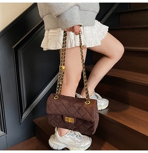 Détail d'un sac bandoulière en velours matelassé marron avec chaîne dorée sur mannequin