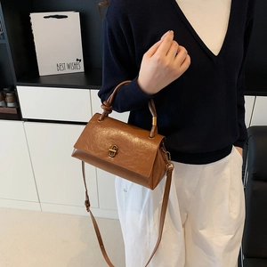 Brown leather crossbody bag with knot handle and gold rotating lock shown on model