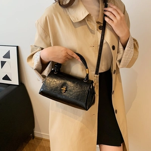 Minimalist black embossed leather crossbody handbag with a circular gold lock and top handle